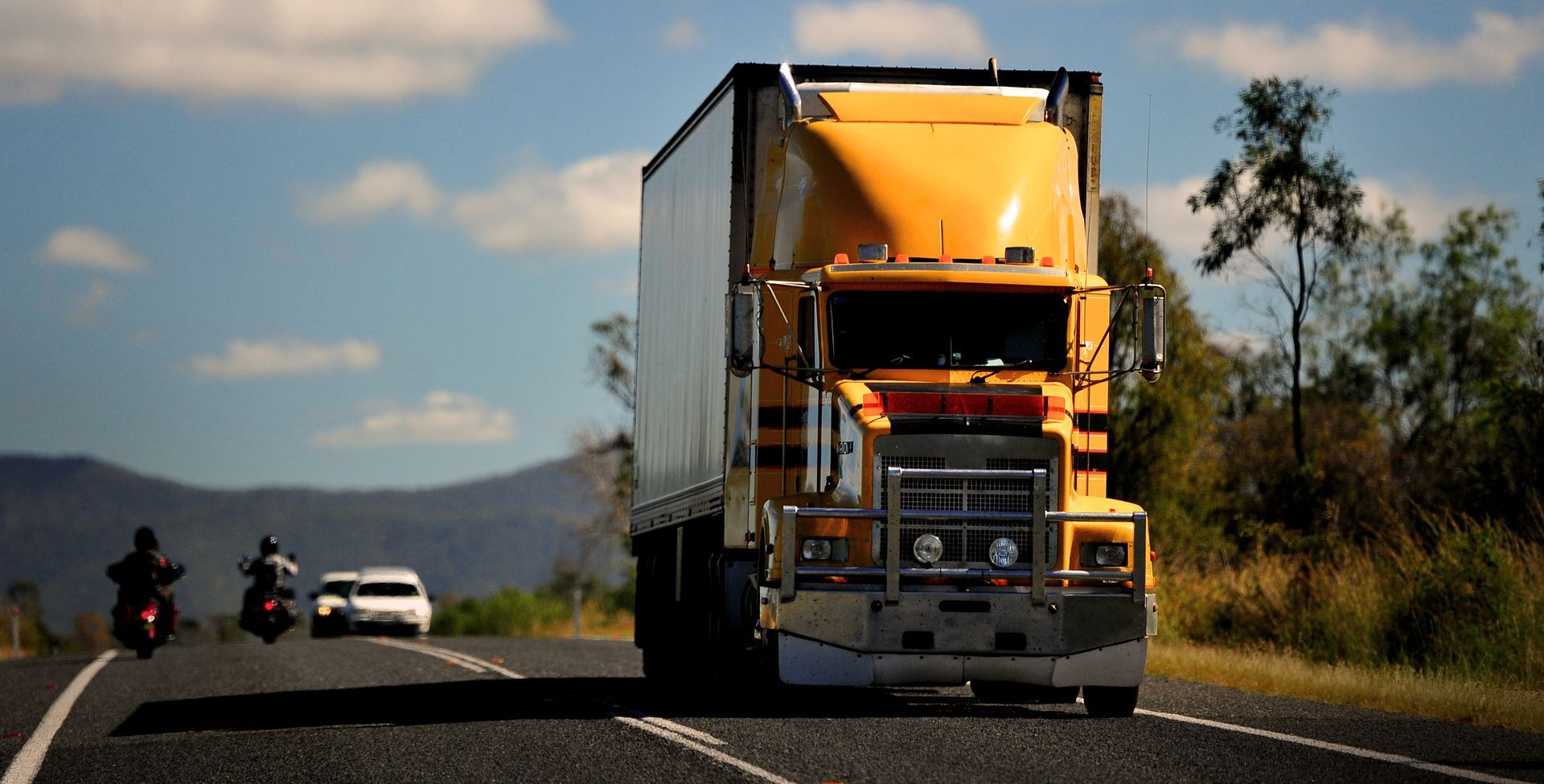 Yellow Semi-truck on a Road, With Motorcycles and Car in Background — Mission Truck Training in Mountain Creek, QLD