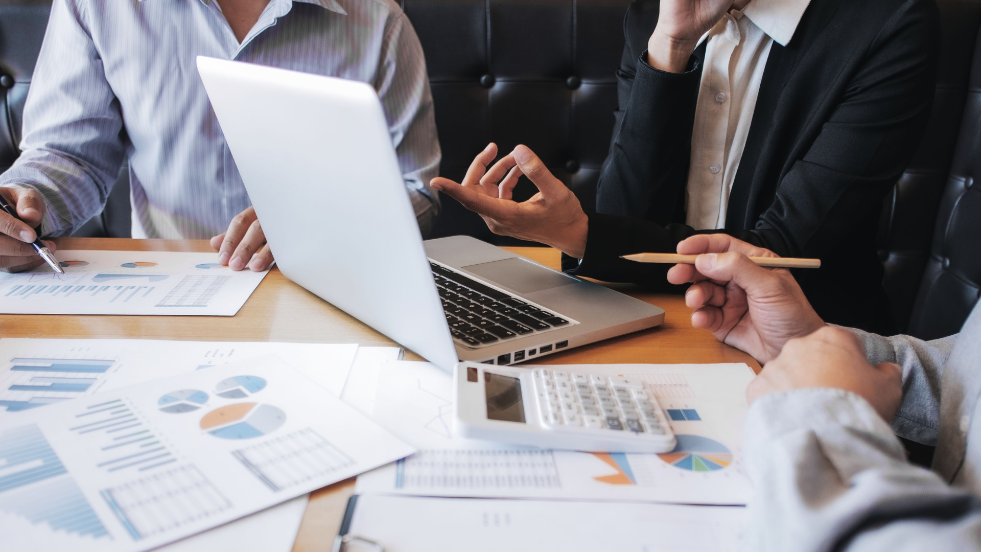 People in a business meeting, reviewing financial data on papers and a laptop.