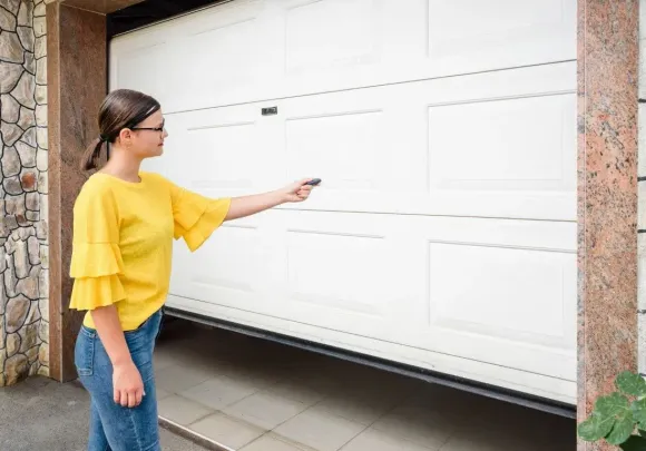 Woman using a remote control to operate a white automatic garage door.