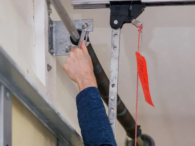 Close-up of a technician using a wrench to adjust garage door hardware.