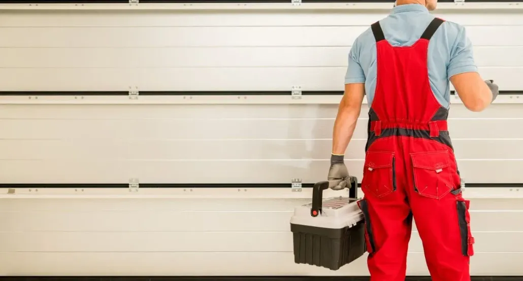 Garage door repairman in red overalls carrying a professional toolbox.
