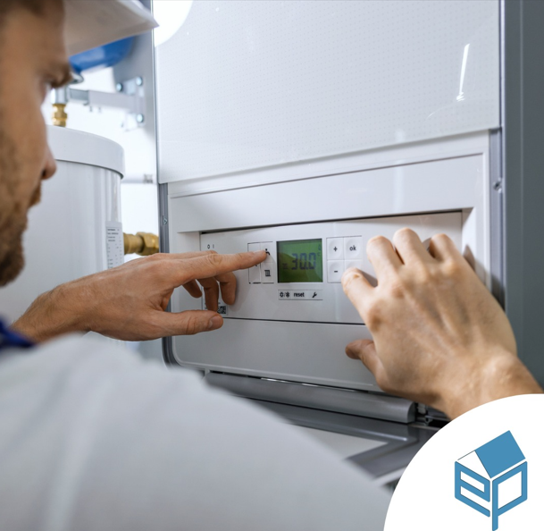 Una persona con indosso un elmetto bianco regola le impostazioni di un pannello di controllo della caldaia montato a parete.
