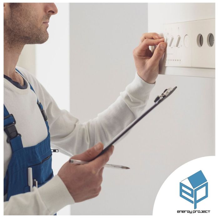 Un tecnico in tuta blu ispeziona un'unità a parete mentre tiene in mano un blocco appunti e una penna.