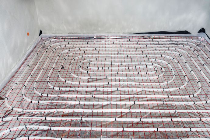 Un sistema di riscaldamento radiante a pavimento in fase di posa, con tubi bianchi disposti a spirale sopra uno strato isolante riflettente grigliato.