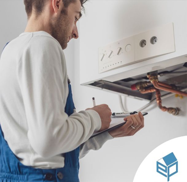 Una persona in tuta blu scrive su un blocco appunti mentre ispeziona l'impianto idraulico di un'unità di riscaldamento a parete.