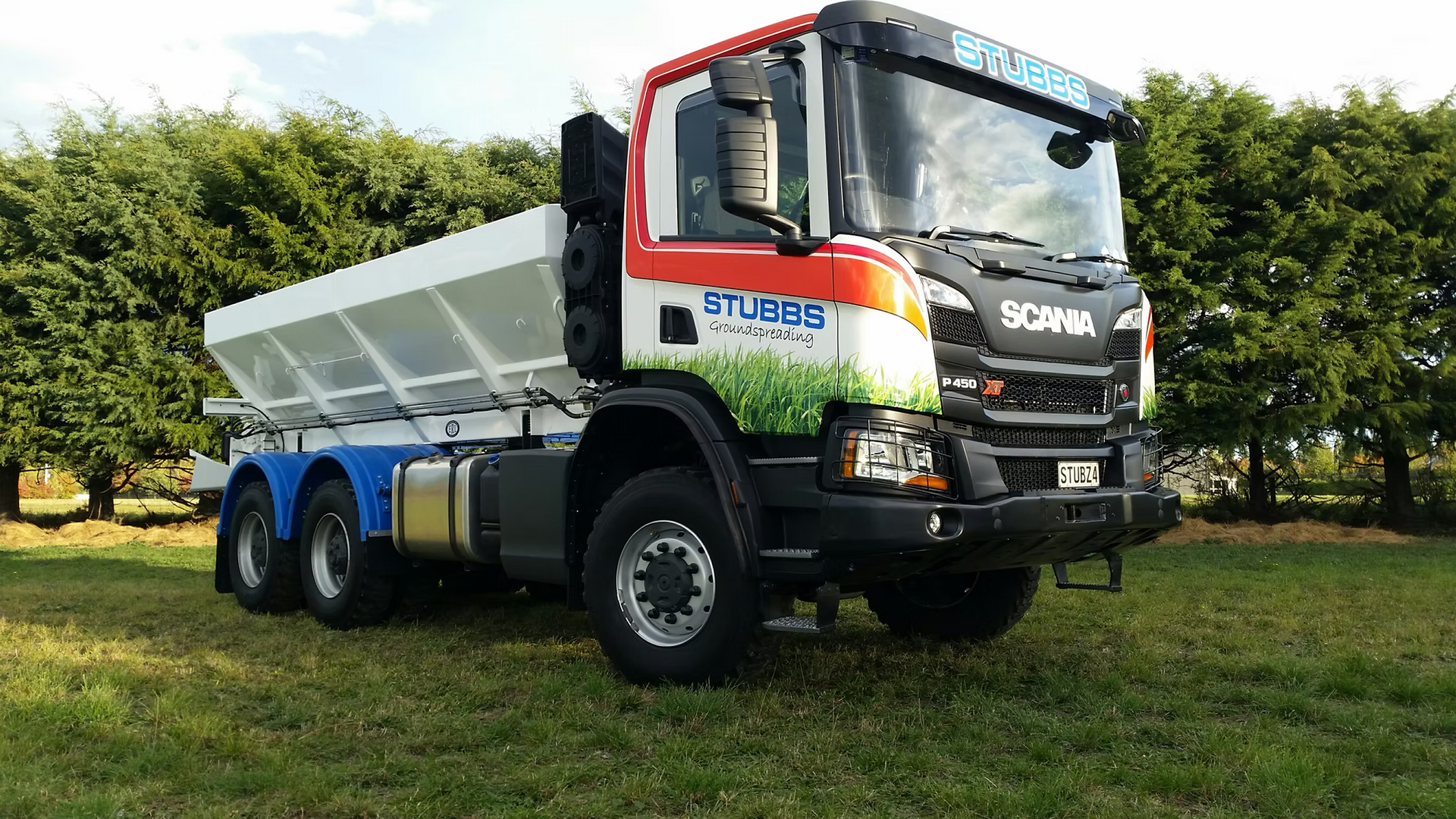 White Scania dump truck parked on grass in front of orchard trees