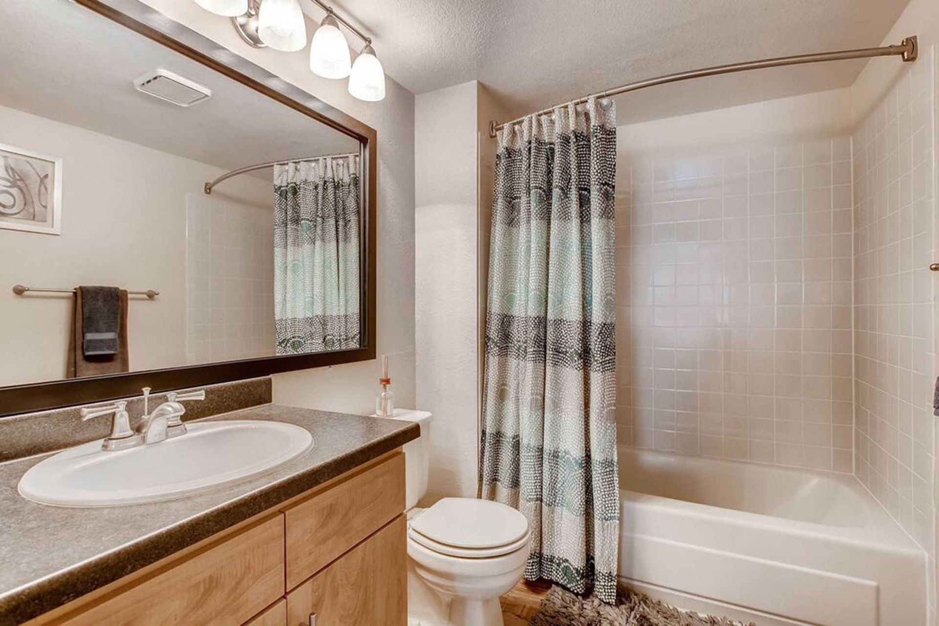 Bathroom with sink, toilet, and bathtub. Shower curtain has black and white pattern at Chestnut Ridge Apartment Homes, offers apartments near Denver Tech Center. Beige walls and cabinetry.