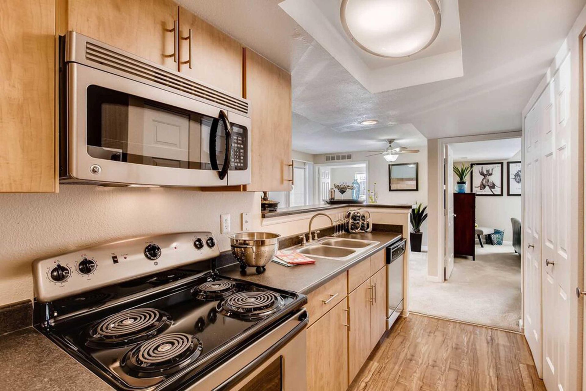 Kitchen with stainless steel microwave, black stovetop, light wood cabinets, sink, and doorway to another room at Chestnut Ridge Apartment Homes, offers apartments in Denver, CO.