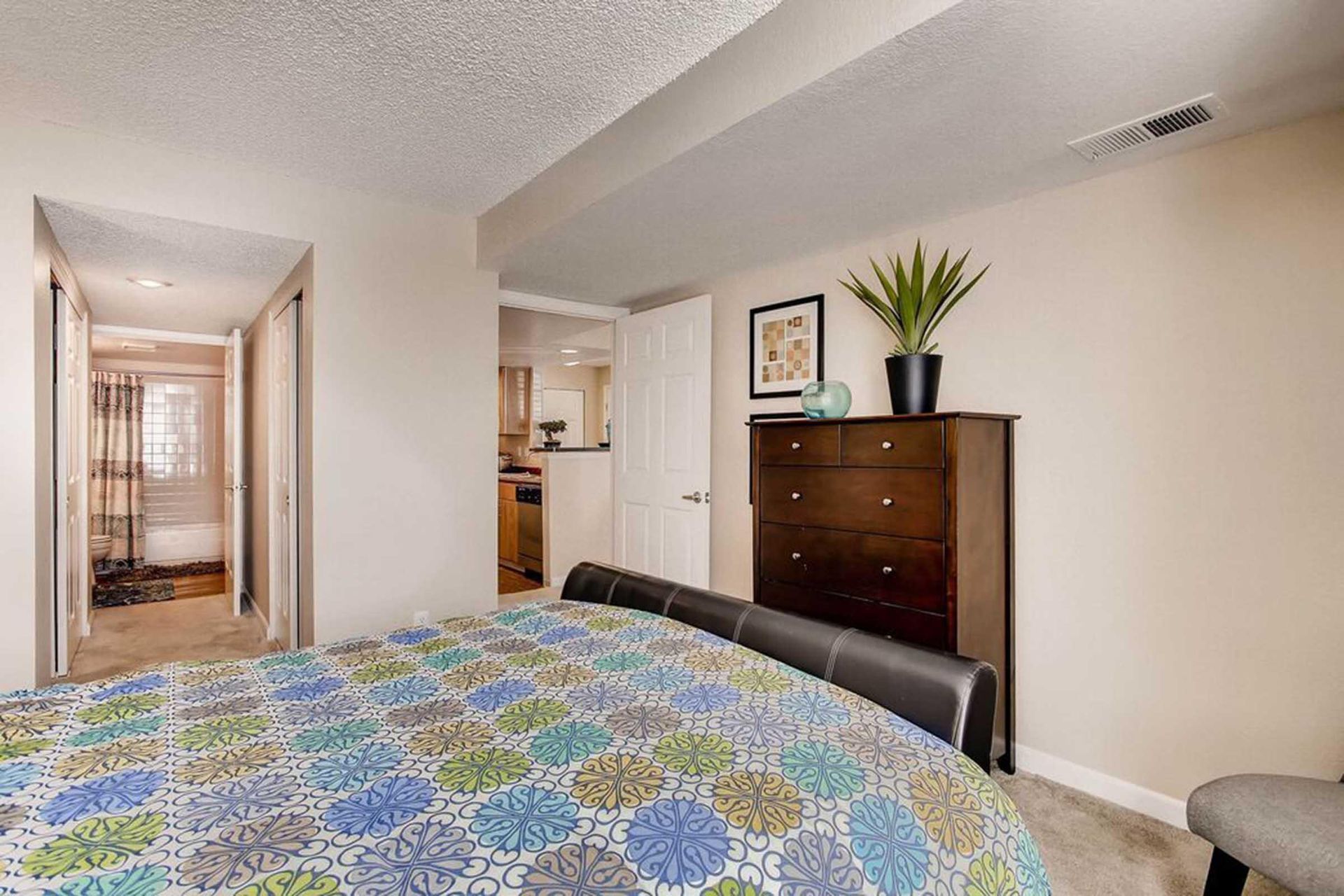 Bedroom with bed, dresser, and a hallway leading to a kitchen at Chestnut Ridge Apartment Homes, offers apartments near Denver Tech Center.