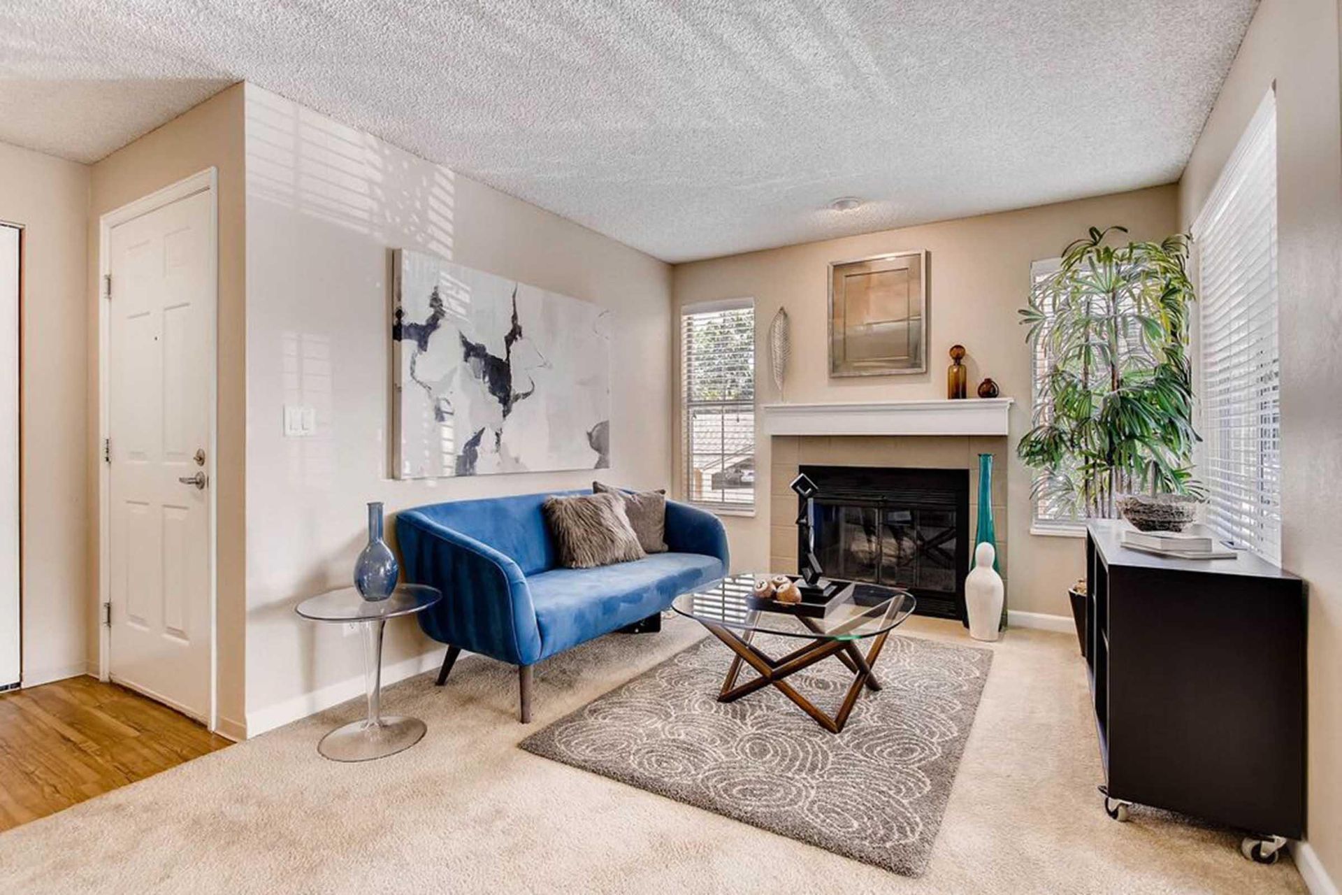 Living room with blue sofa, fireplace, and abstract art; neutral color palette.
