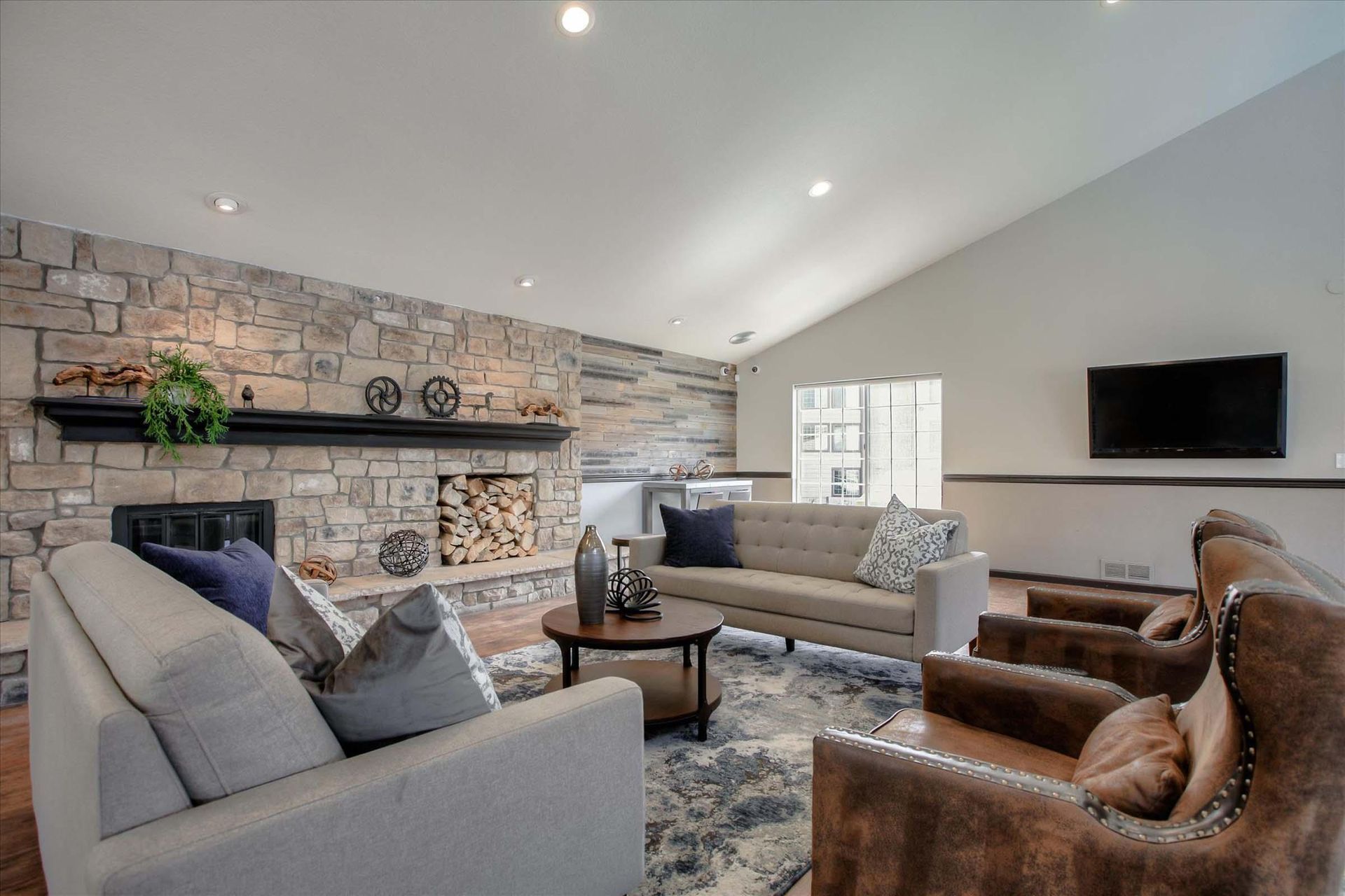 Clubhouse with stone fireplace, gray couches, and a TV on the wall at Chestnut Ridge Apartment Homes, offers pet-friendly apartments for rent in Denver, CO.