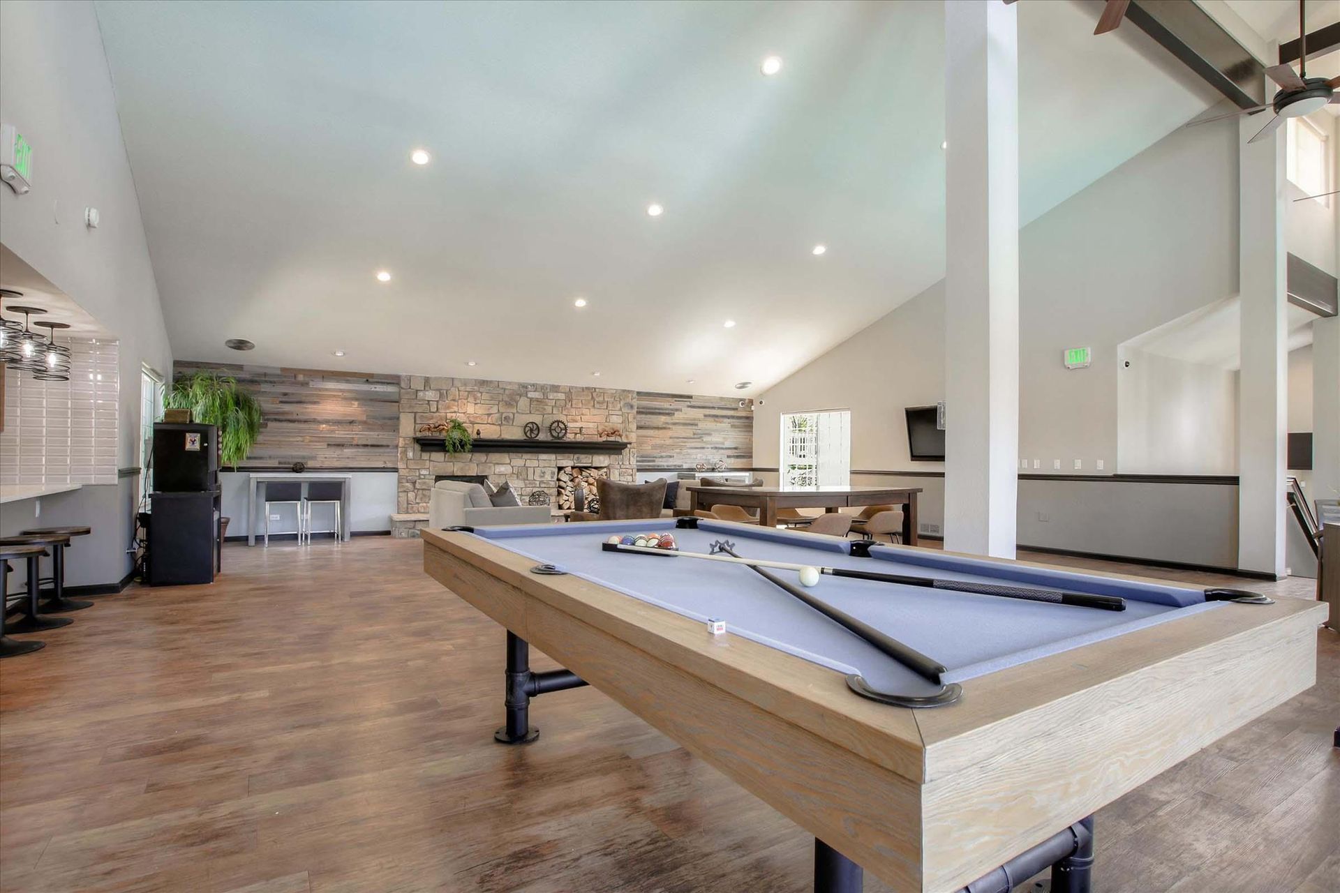 Pool table in a spacious rec room with high ceilings, fireplace, and hardwood floors.