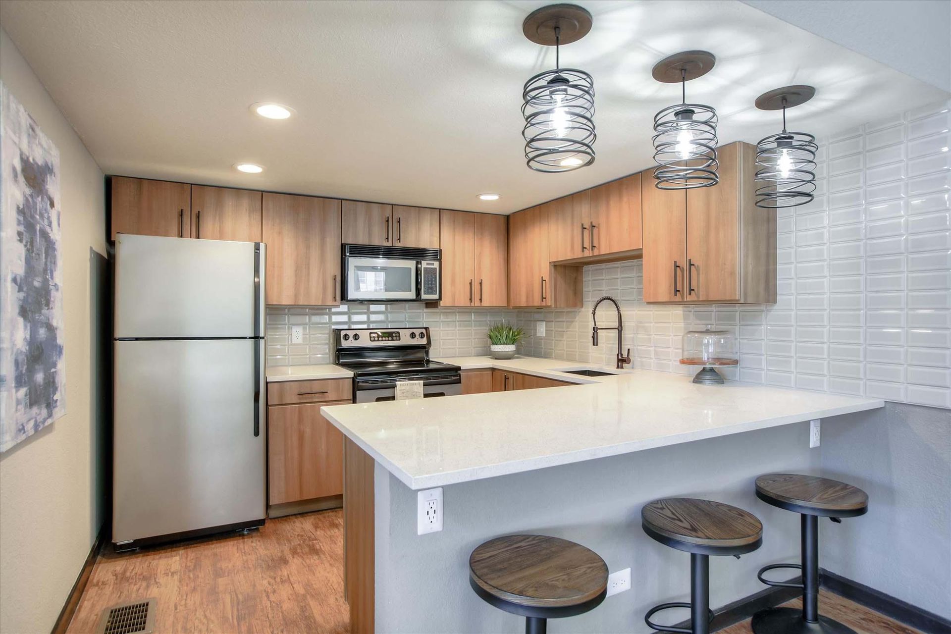 Kitchen with light wood cabinets, stainless steel appliances, breakfast bar with stools, and pendant lights at Chestnut Ridge Apartment Homes, offers pet-friendly apartments for rent in Denver, CO.