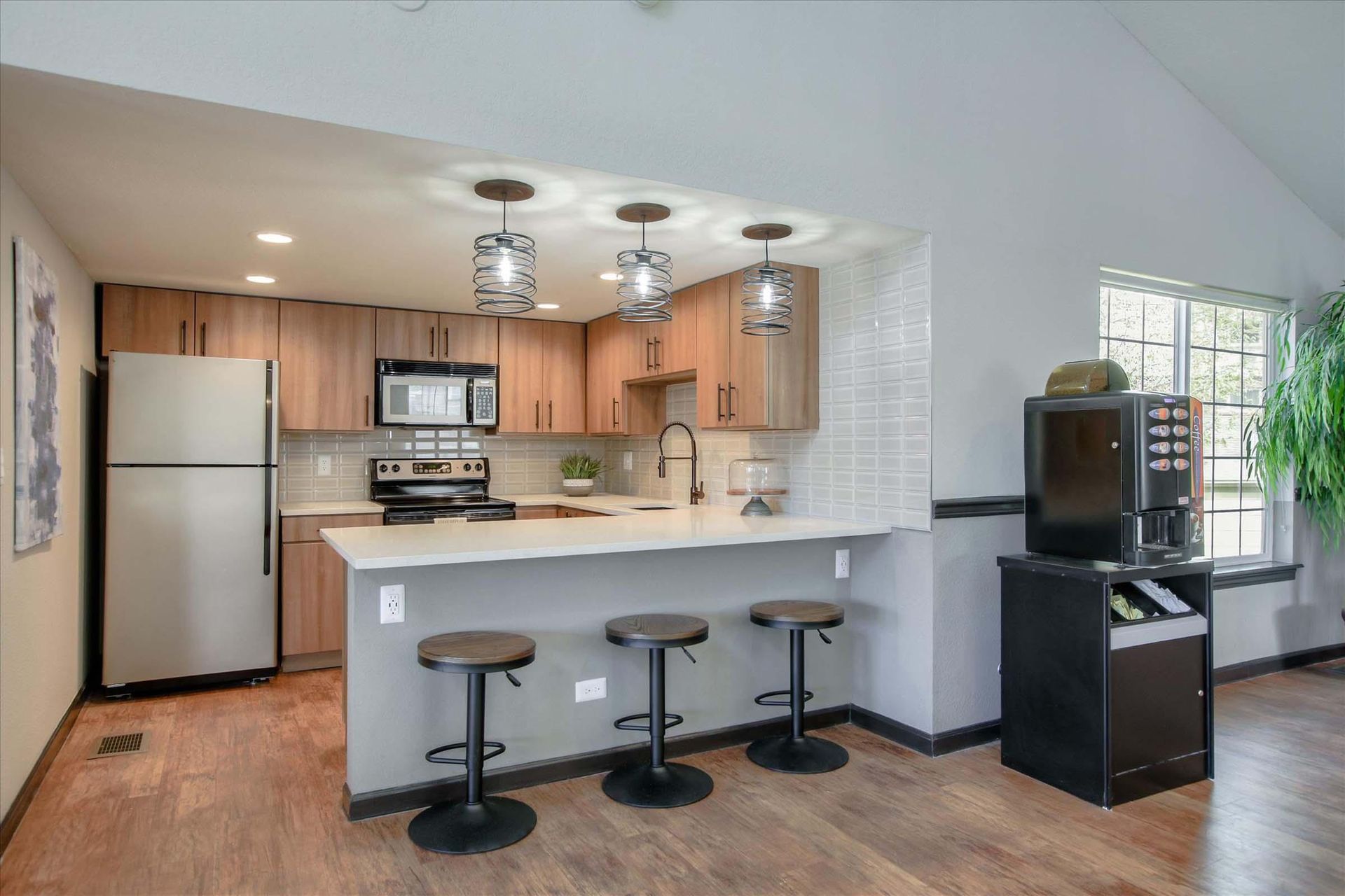 Kitchen with wood cabinets, breakfast bar, stools, stainless steel appliances, and pendant lights at Chestnut Ridge Apartment Homes, offers apartments in Denver, CO.