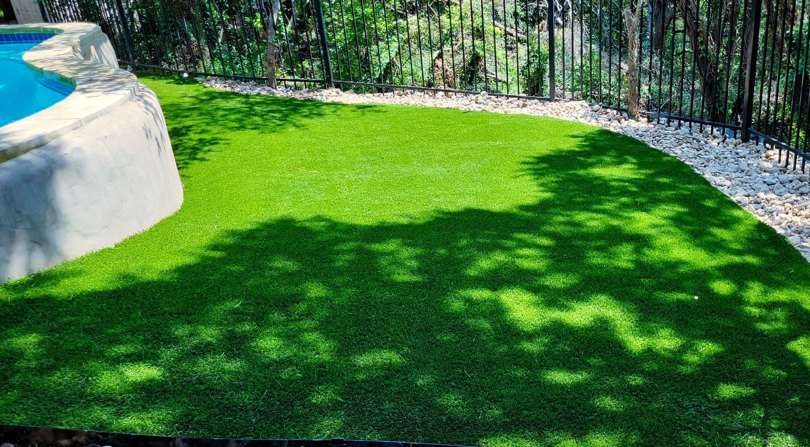 A lawn with a pool in the background and a fence around it.