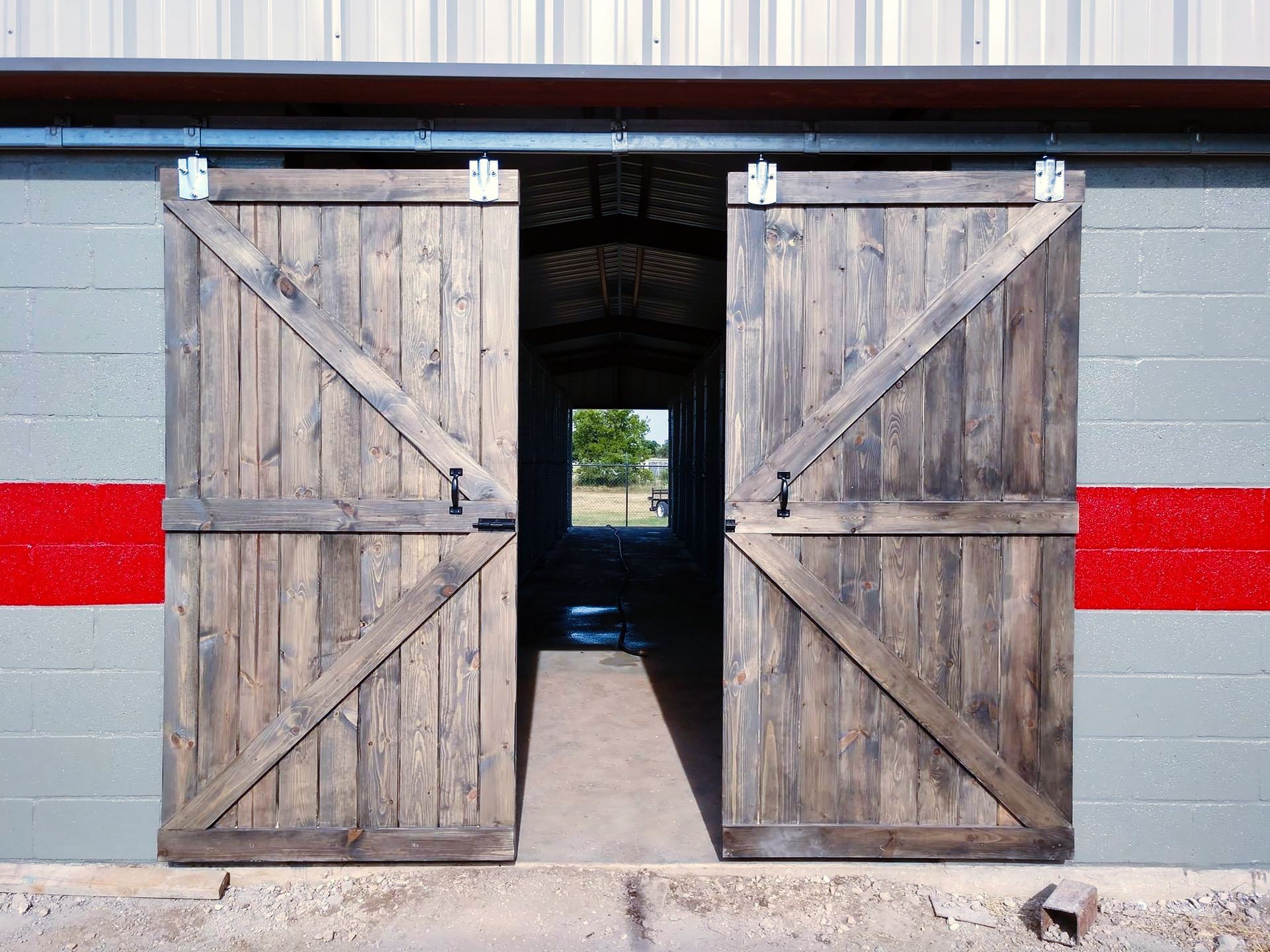 A barn with sliding wooden doors and a red stripe on the side