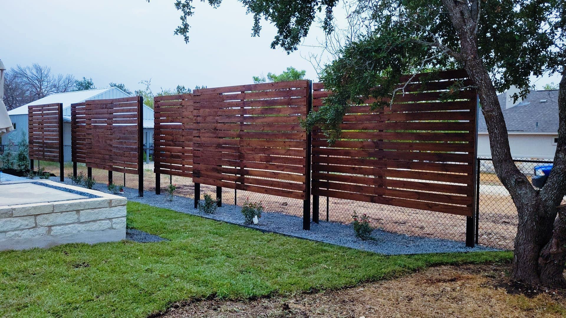 A wooden fence is in the middle of a lush green yard.
