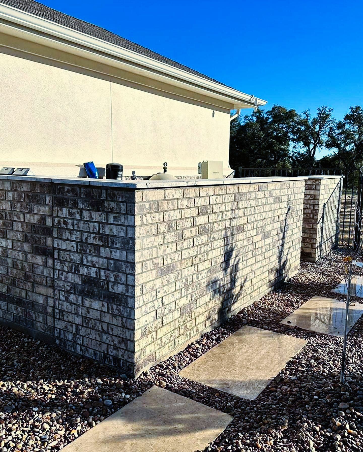 A brick wall surrounds a house with a blue sky in the background.