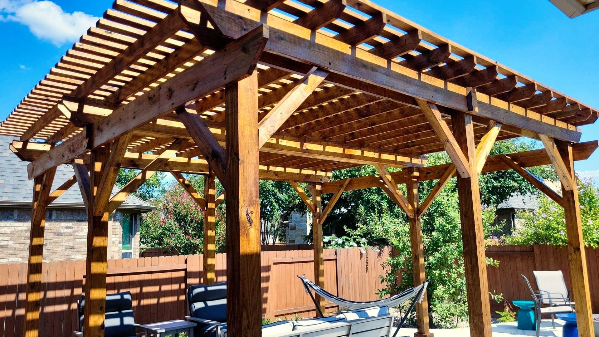 A wooden pergola with a hammock underneath it in a backyard.