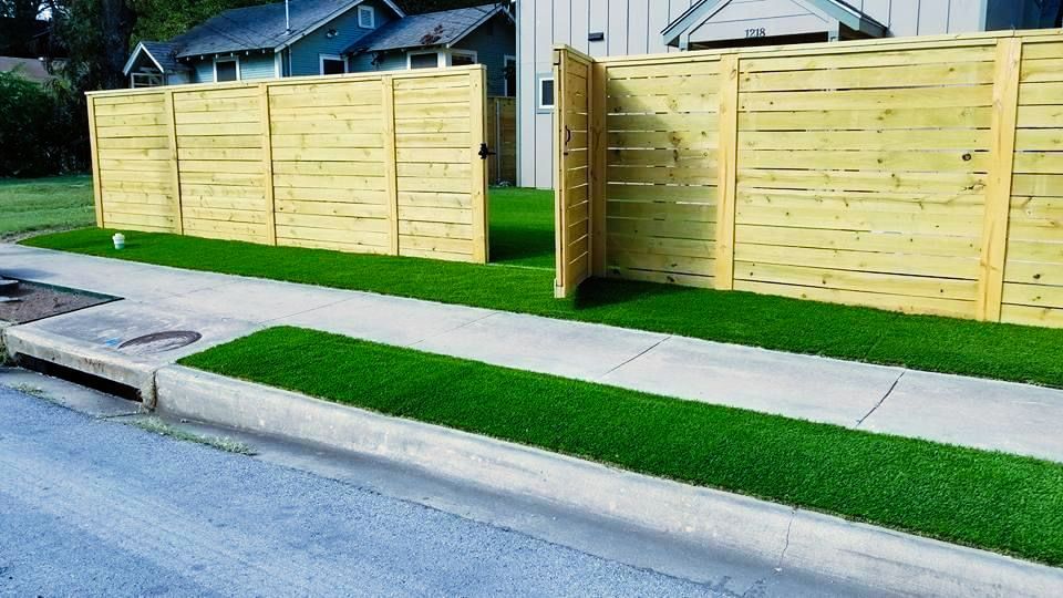 A wooden fence with artificial grass in front of a house.