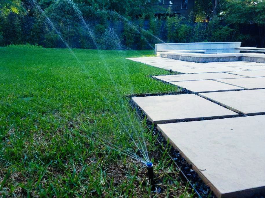 A lawn sprinkler is spraying water on a lush green lawn