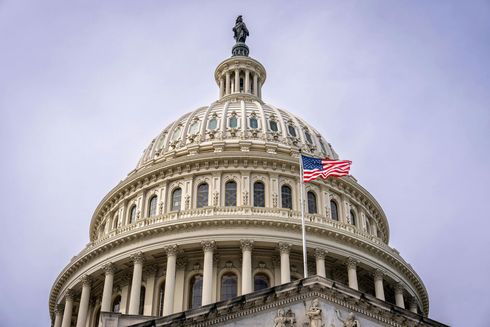 The United States Capitol dome with American flag waving on a cloudy day.