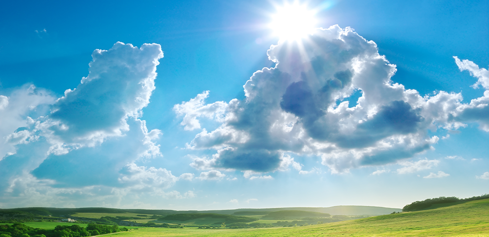 The sun is shining through the clouds over a green field.