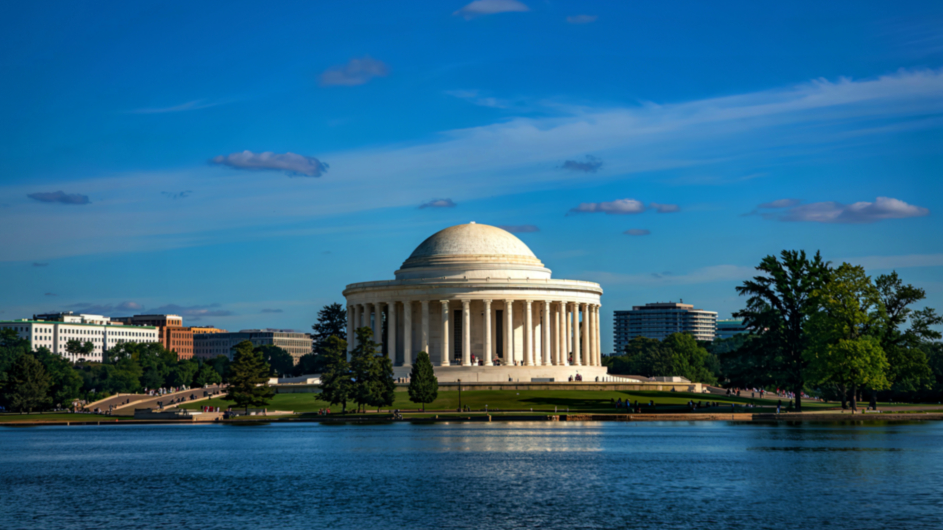 Thomas Jefferson Memorial, white marble, beside a calm blue lake, under a blue sky.