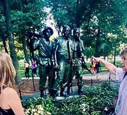 Bronze statue of three soldiers in a park; woman points at them.