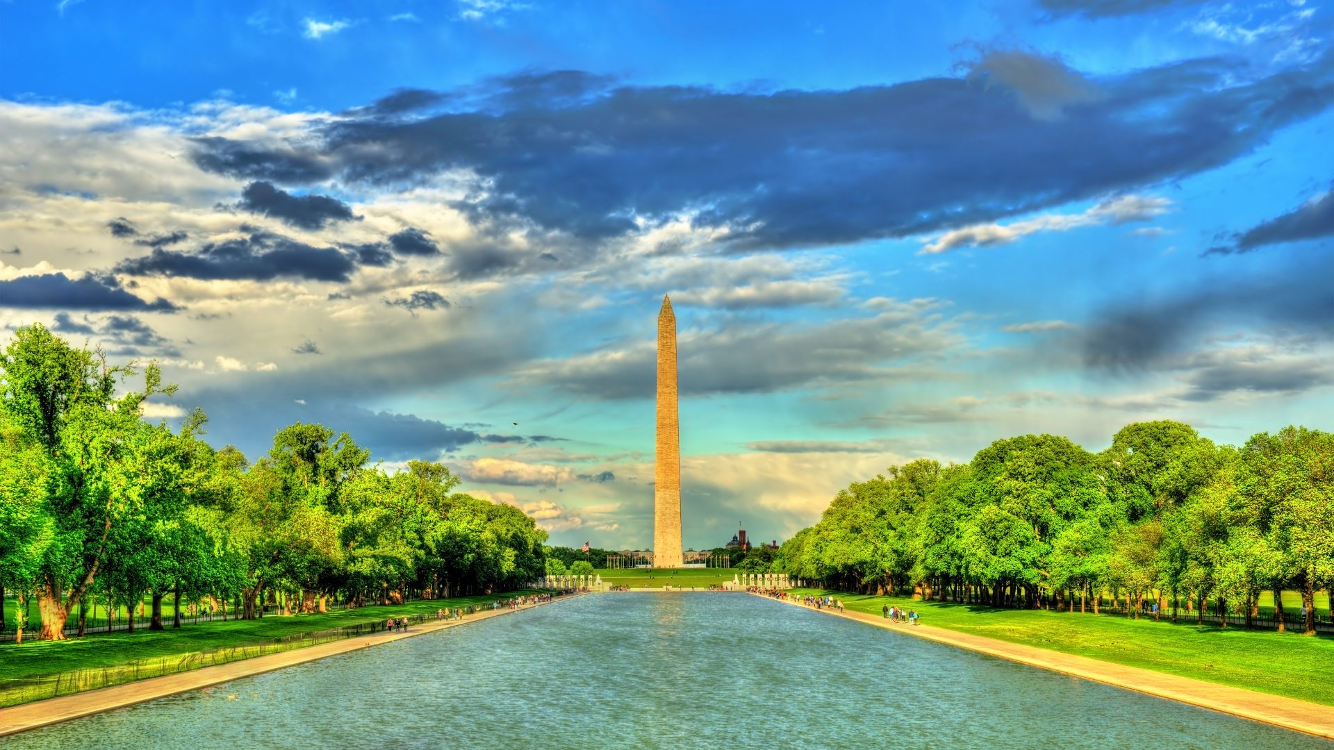 Washington Monument, reflecting pool, surrounded by trees under a dramatic, cloudy sky.