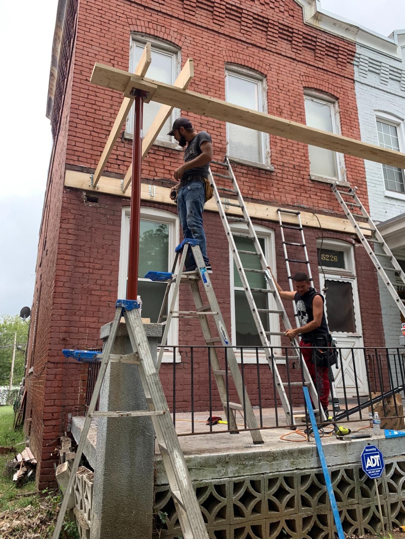 Two men are standing on ladders in front of a brick building.