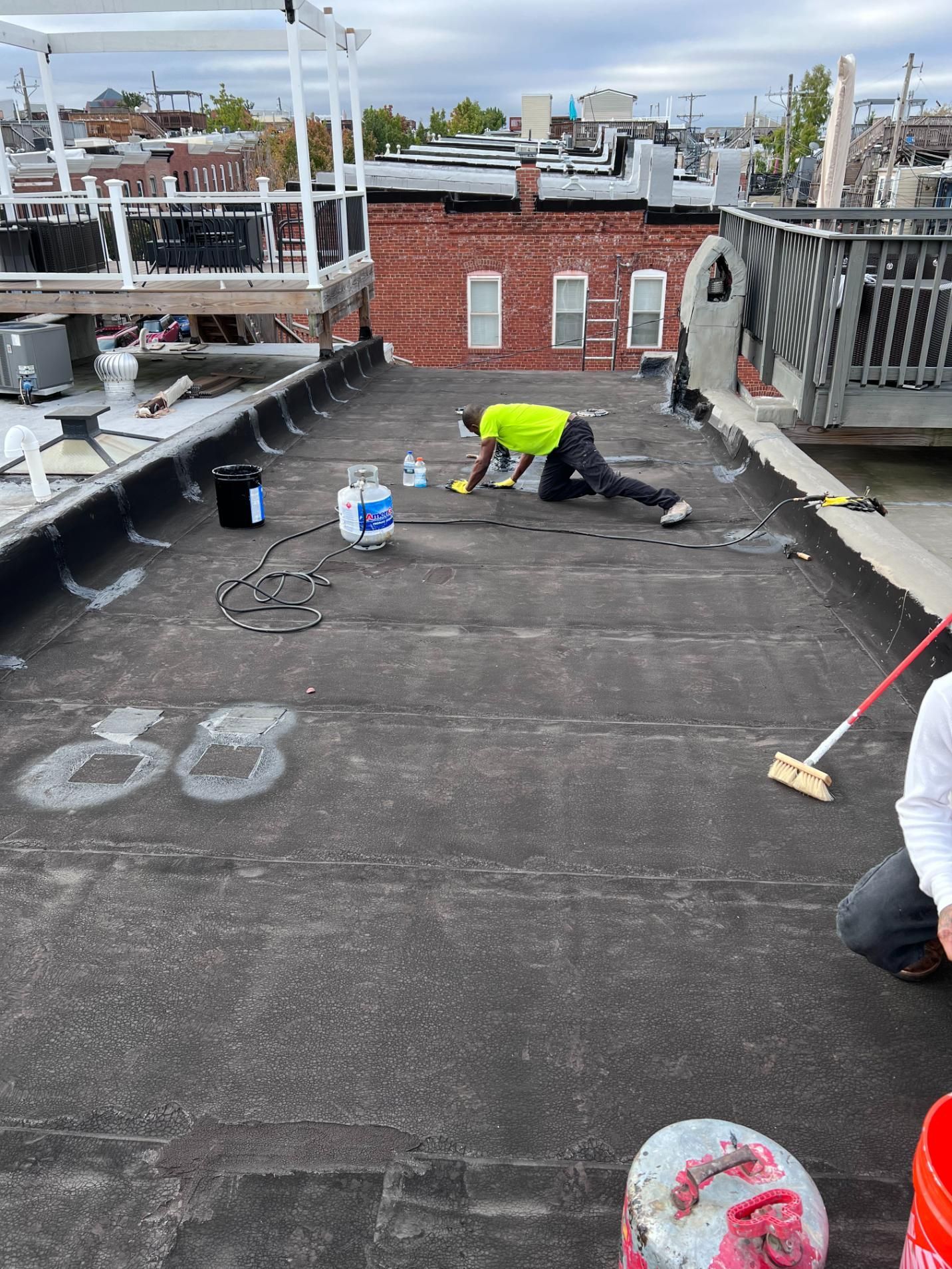 A man is kneeling on a roof with a broom.