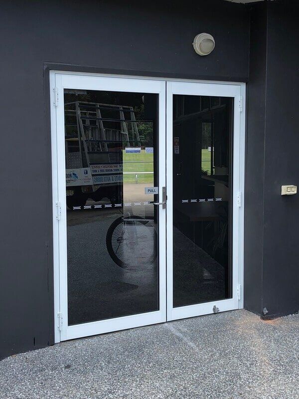 Dark storefront with white-framed glass double doors and a round wall light above.