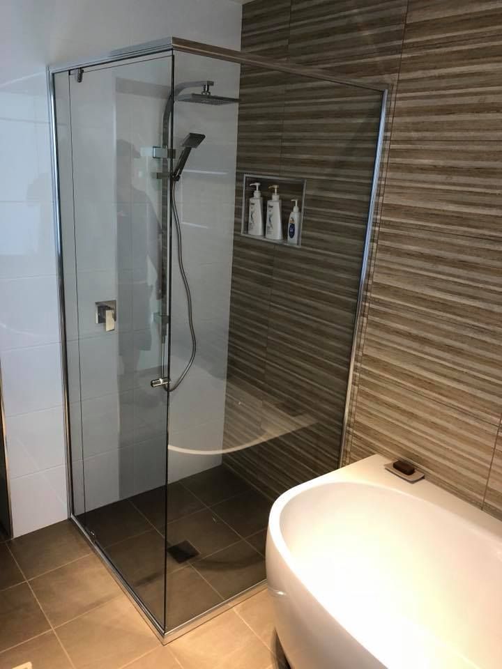 Modern bathroom with glass shower enclosure, tiled walls, and a white sink in the foreground