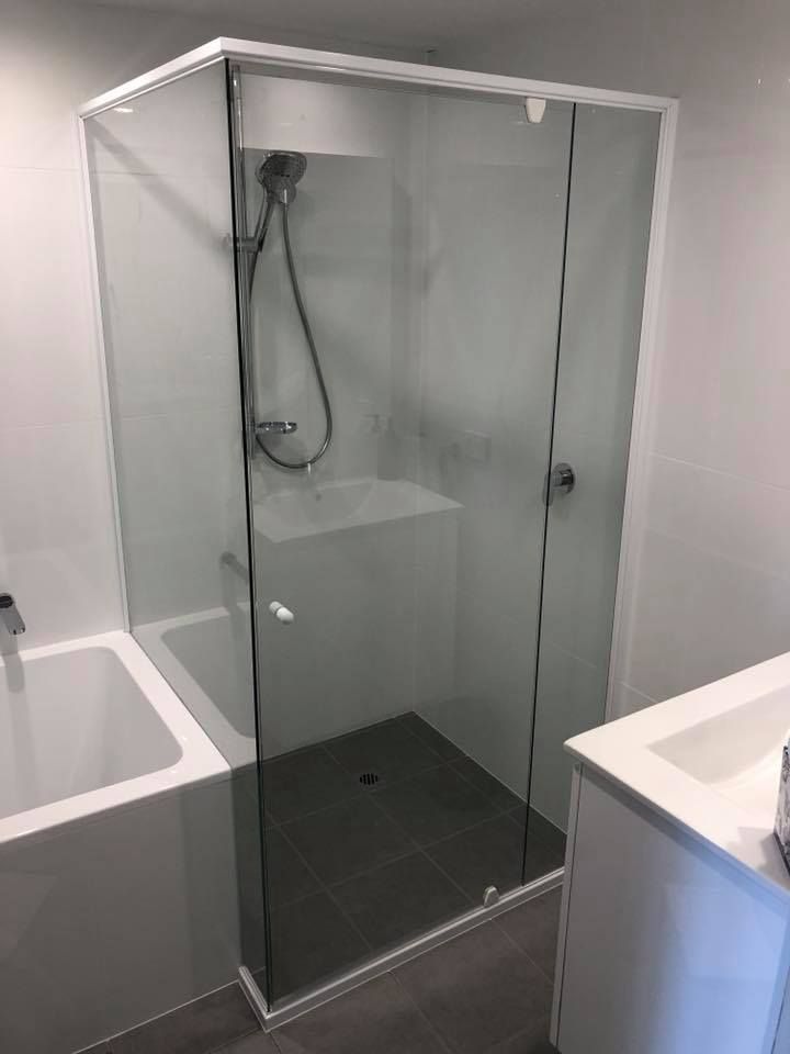 Glass shower enclosure in a modern bathroom with gray tile and white fixtures