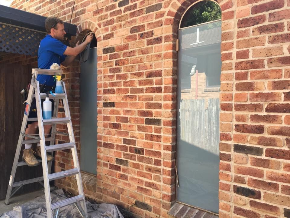 Worker on ladder installing a dark panel beside a brick wall and arched window