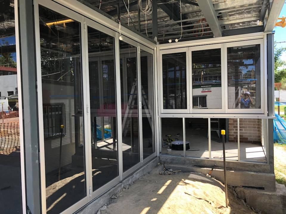 Partially enclosed patio under construction with white-framed glass walls and a concrete floor