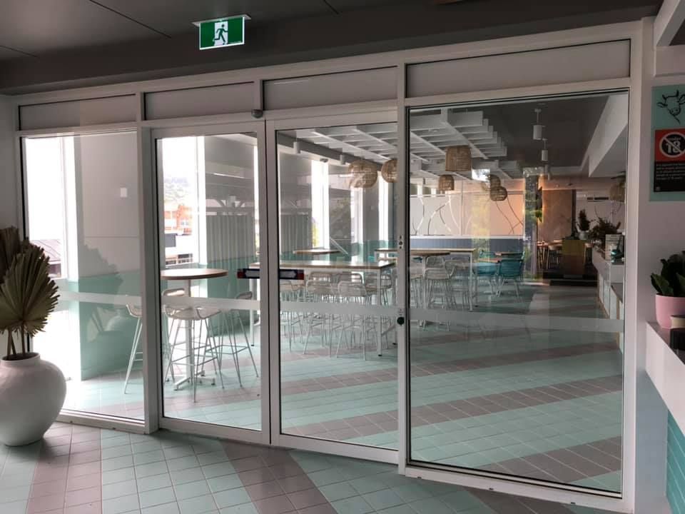 Empty glass doors leading to a bright indoor seating area with green chairs and tables