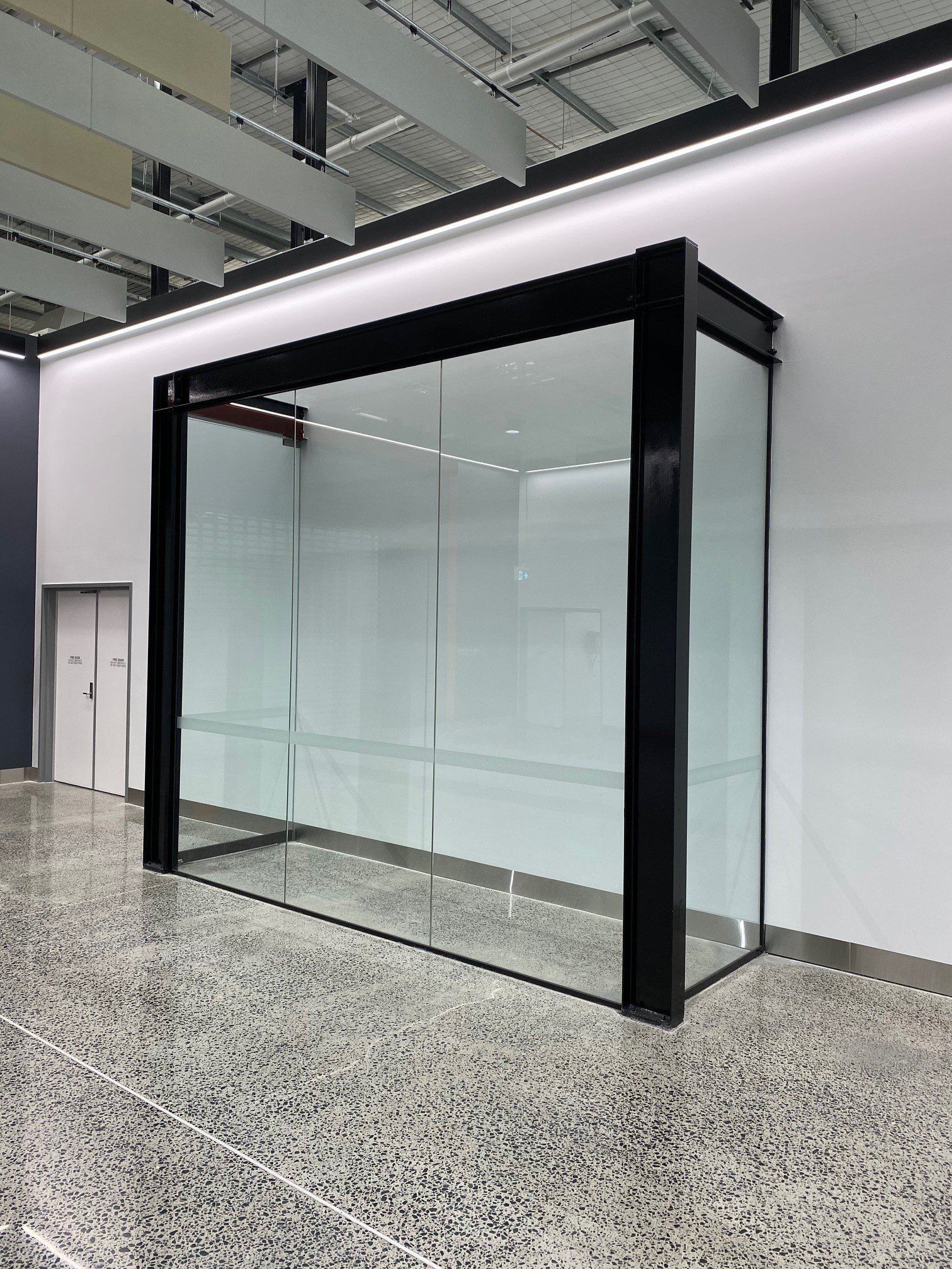 Empty glass storefront display in a modern indoor corridor with black framing and white walls
