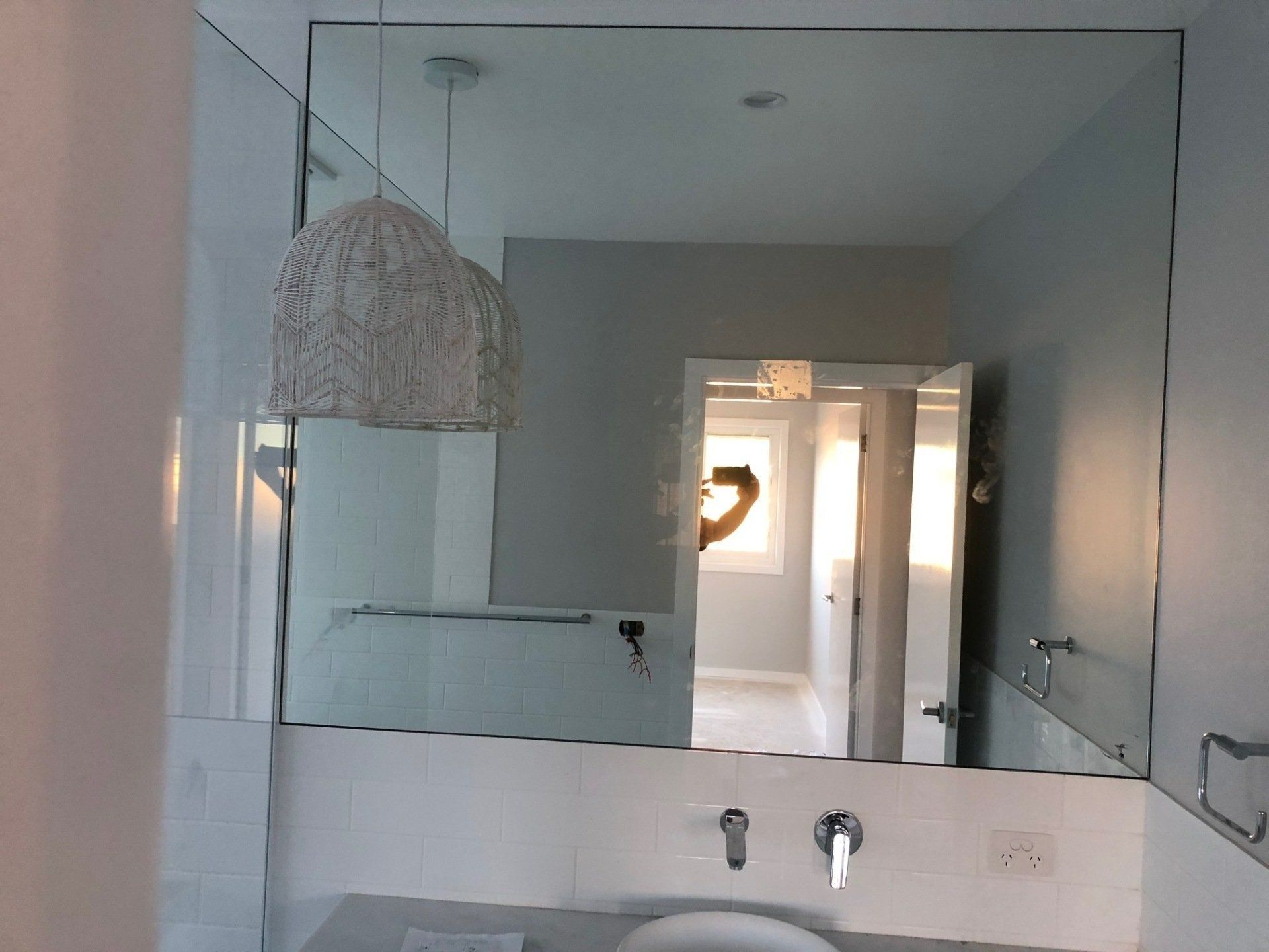 Bathroom mirror above sink with pendant light and hallway reflected in the glass