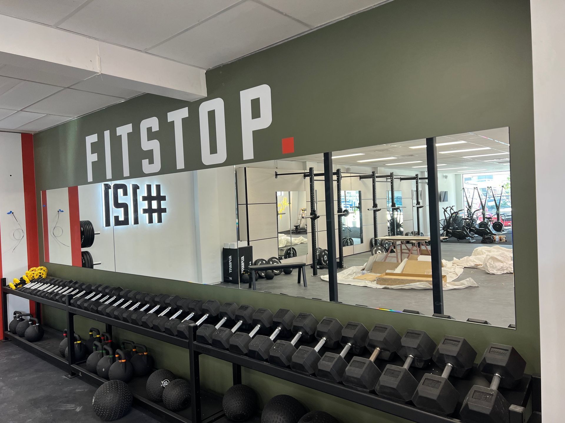 Gym interior with dumbbell rack, medicine balls, and mirrored wall under FITSTOP signage