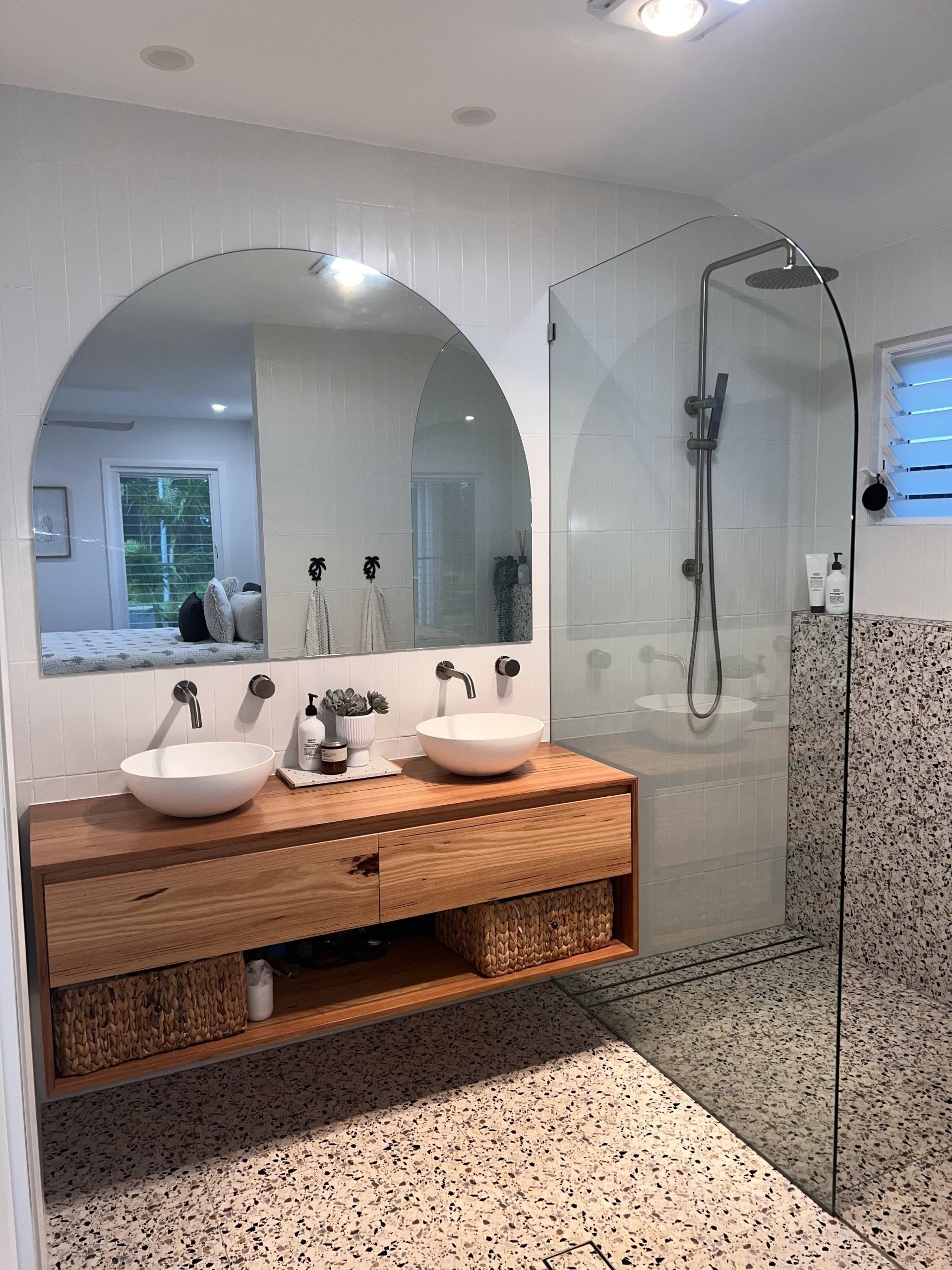 Modern bathroom with double sinks, large mirror, wicker vanity, and glass shower over terrazzo floor.