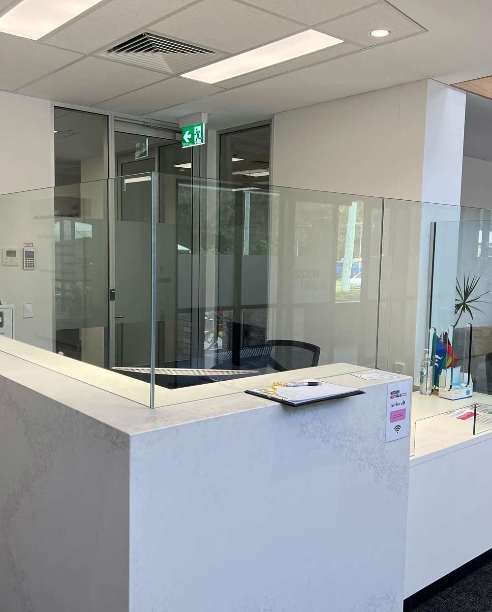 Modern office reception area with glass partitions, white desks, and a notebook on the counter