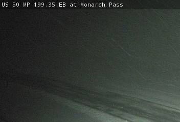 Dark webcam view of US 50 at Monarch Pass.  Snowy road surface. Poor visibility.
