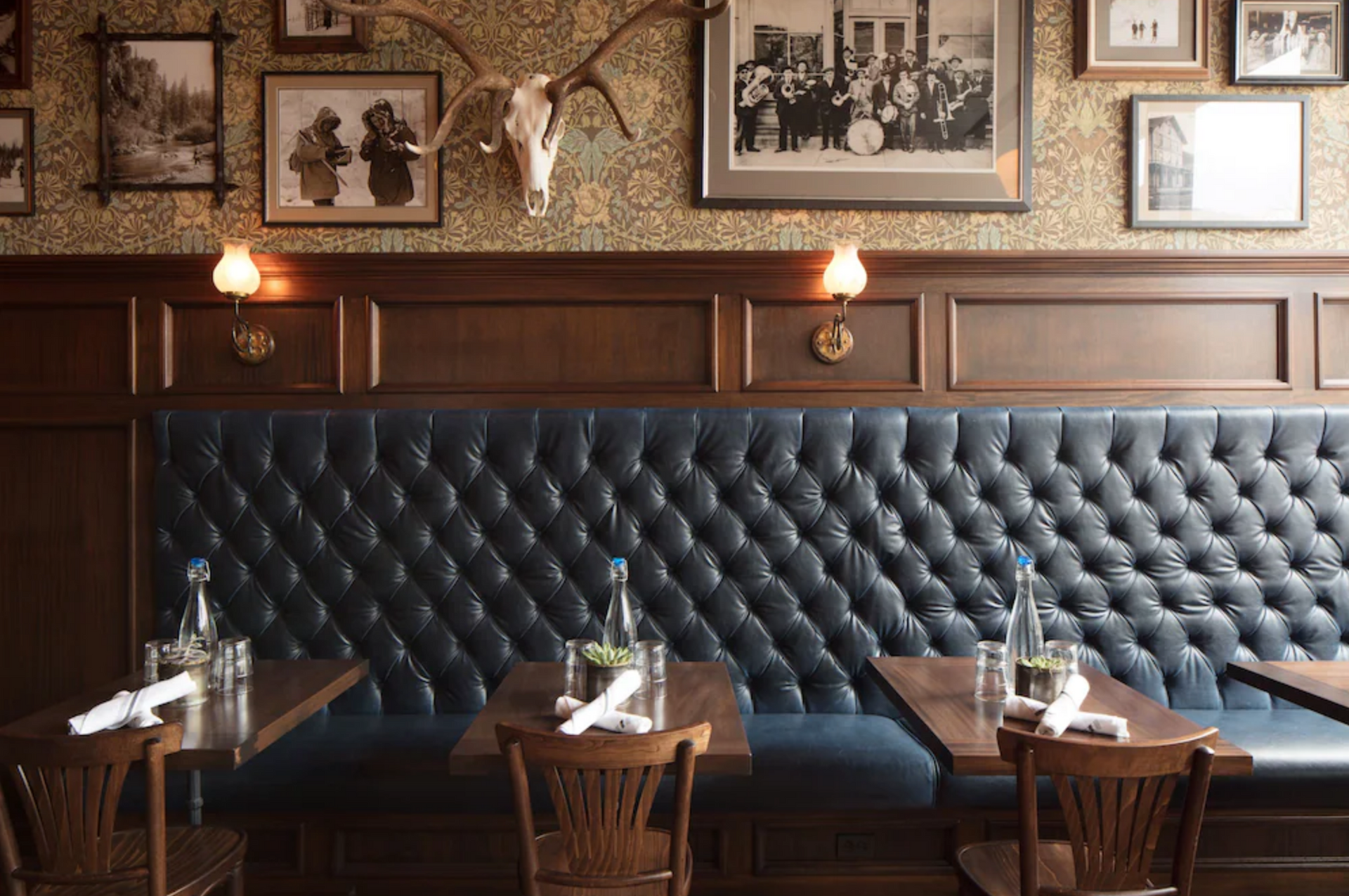 Restaurant booth: blue tufted leather, dark wood paneling, framed art, wood tables and chairs.