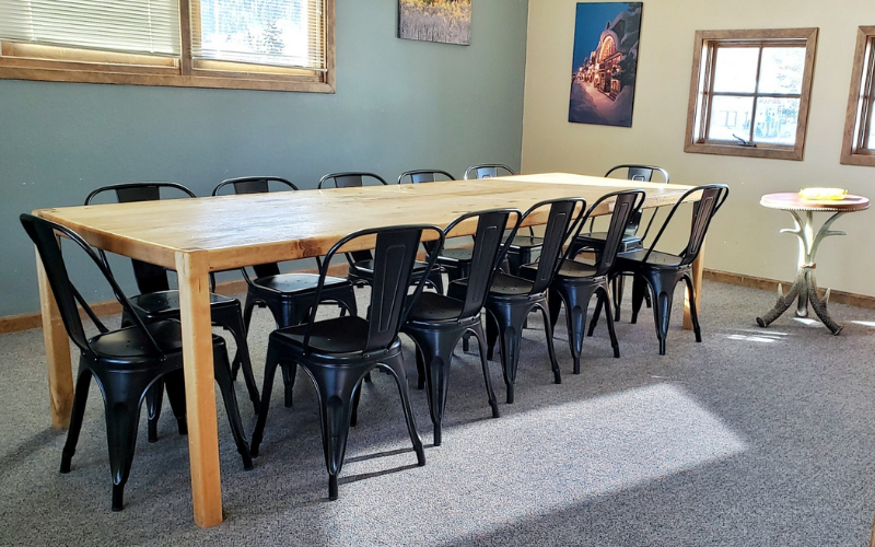 Long wooden table with black chairs in a room with blue walls and sunlight.