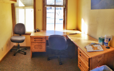 A small office with a large wooden desk, two chairs, and a window with blinds.