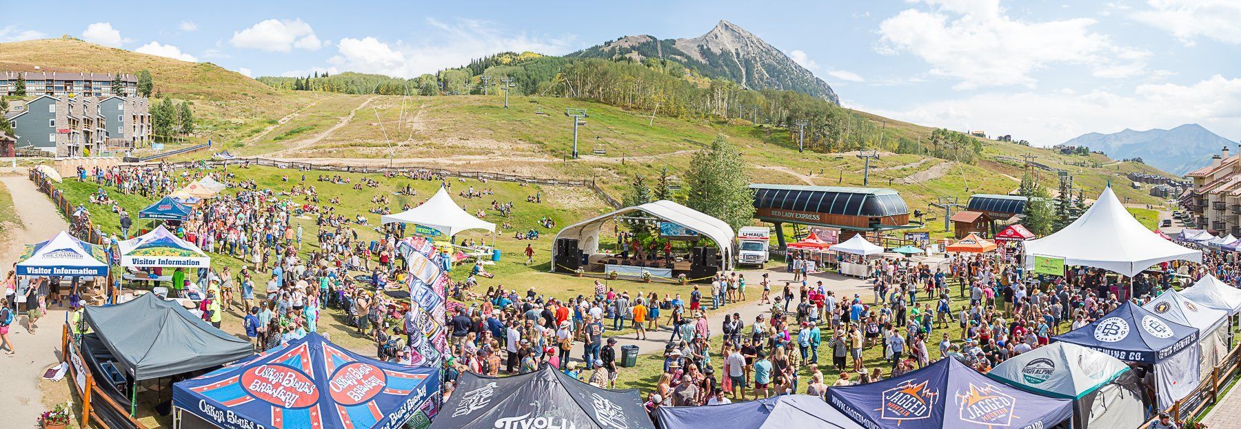 A large outdoor event with tents and crowds, set against a mountain backdrop.