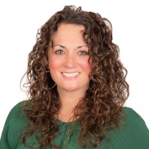 Woman with curly brown hair smiles in a green top against a white background.