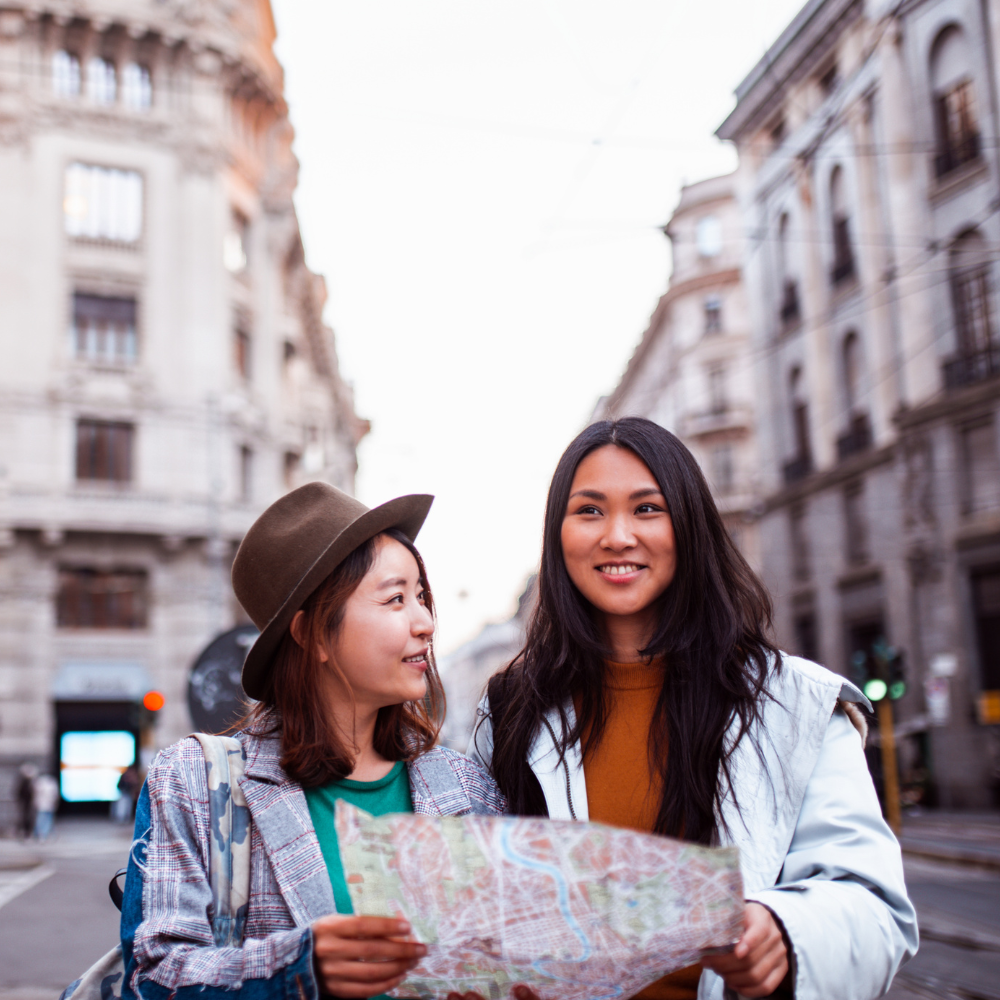Two people holding a map while standing on a European city street, smiling and looking in the same direction.